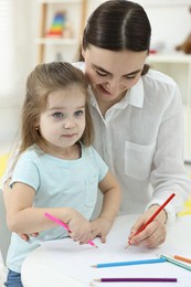 Photo of Mother and her little daughter drawing with colorful pencils at home