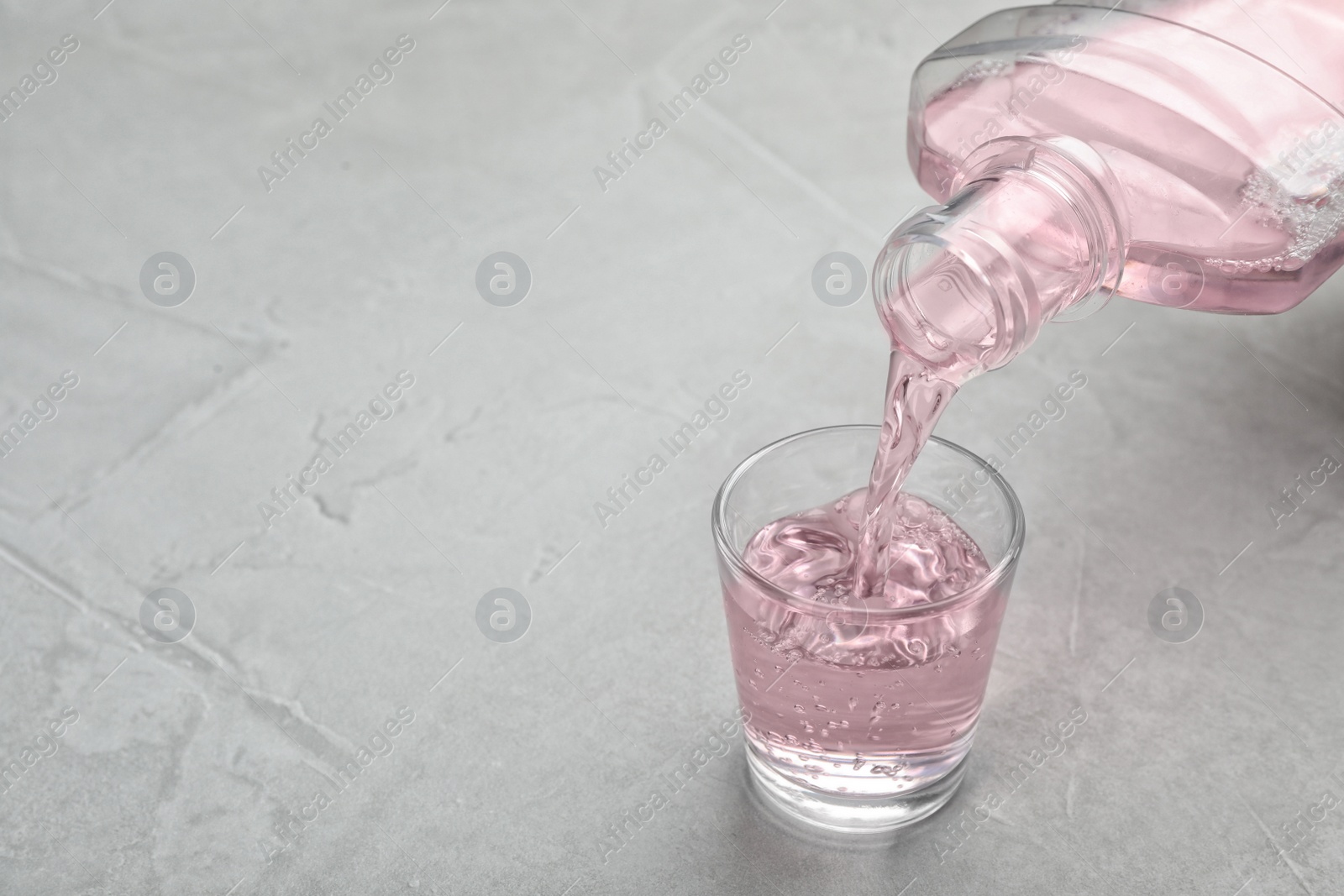 Photo of Pouring mouthwash in glass and space for text on light background. Teeth hygiene