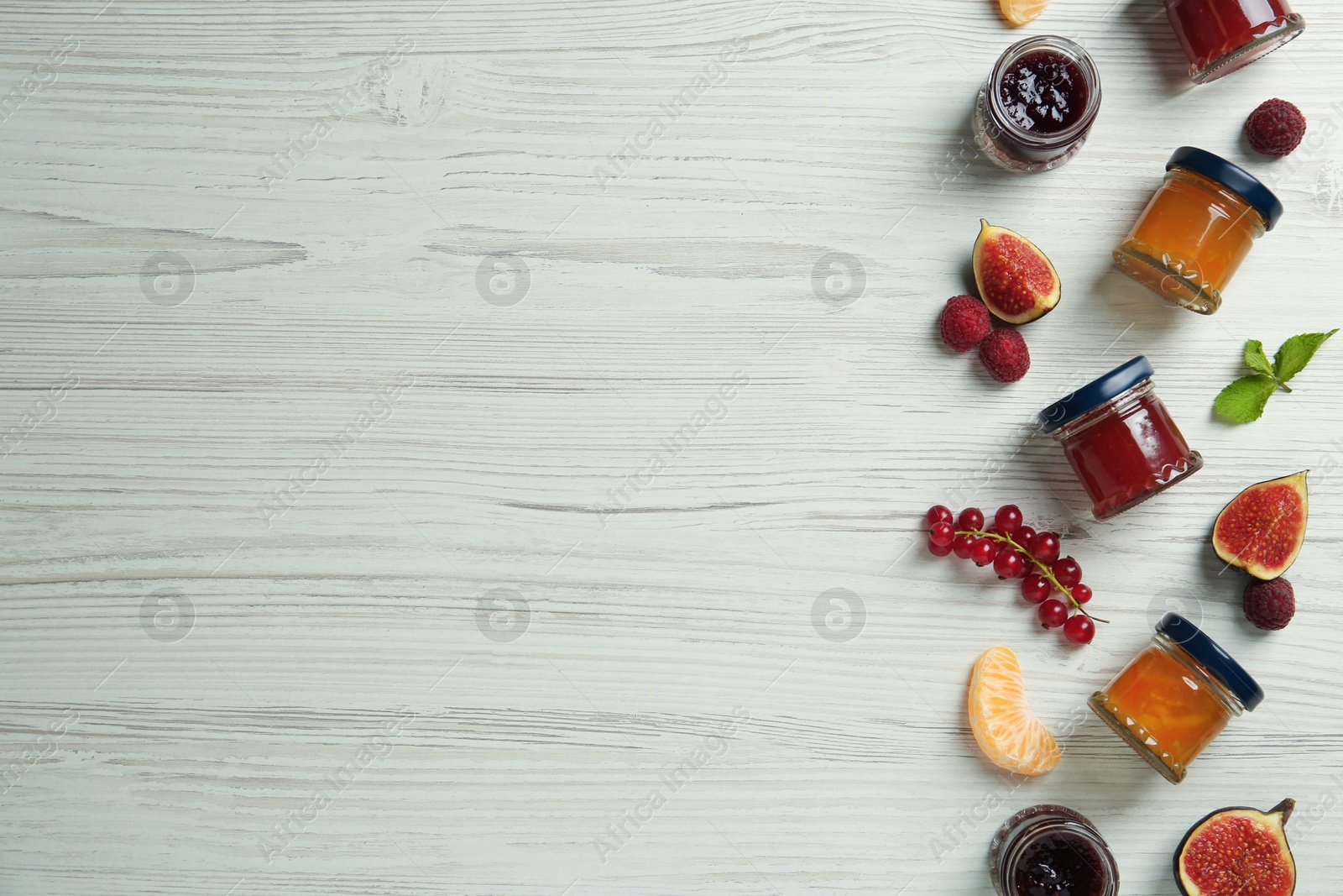 Photo of Jars of different jams and fresh ingredients on white wooden table, flat lay. Space for text