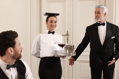 Photo of Senior man wearing formal suit teaching trainees in hotel. Professional butler courses