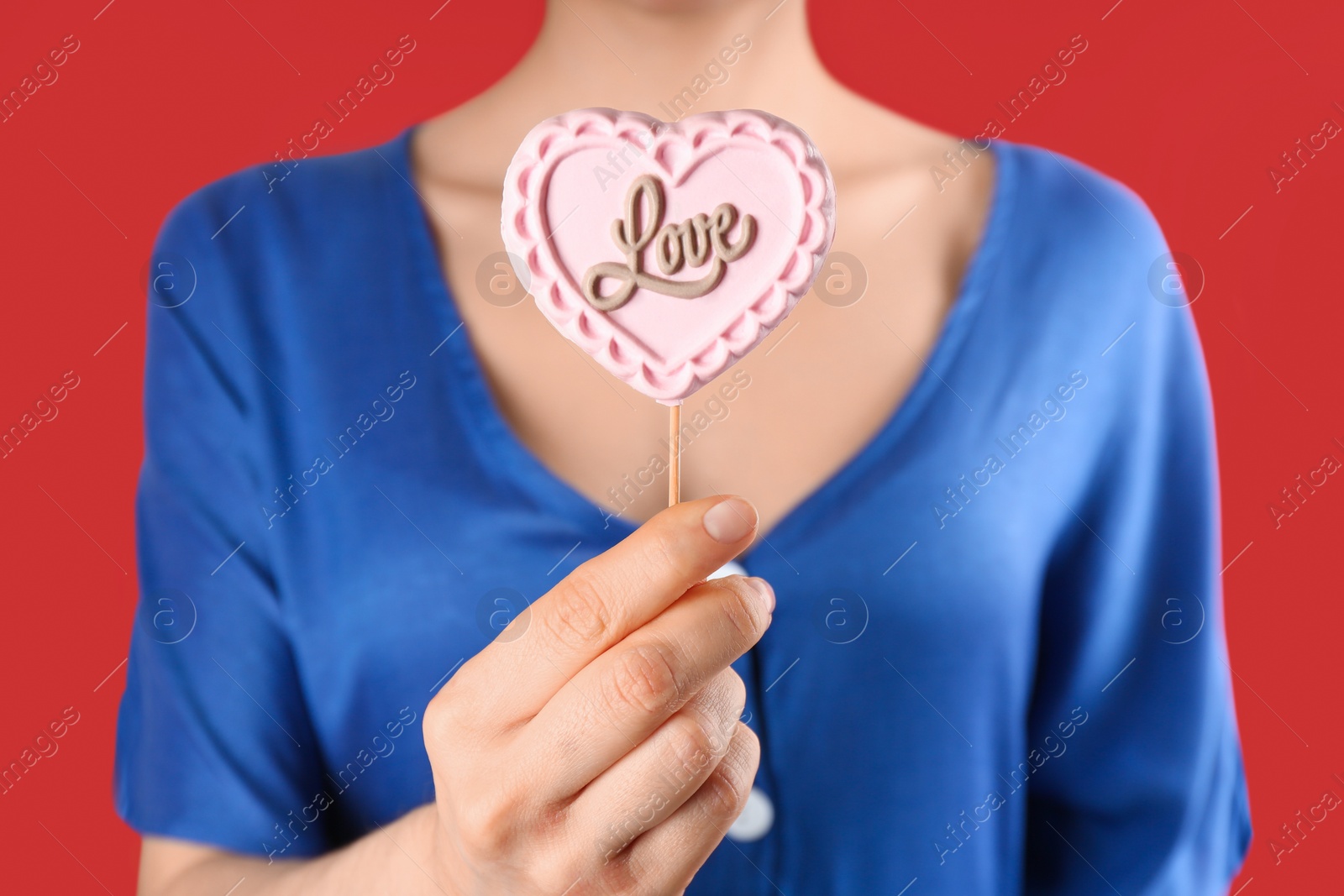 Photo of Woman holding heart shaped lollipop made of chocolate on red background, closeup