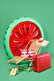 Deck chair, suitcase and beach accessories on green background