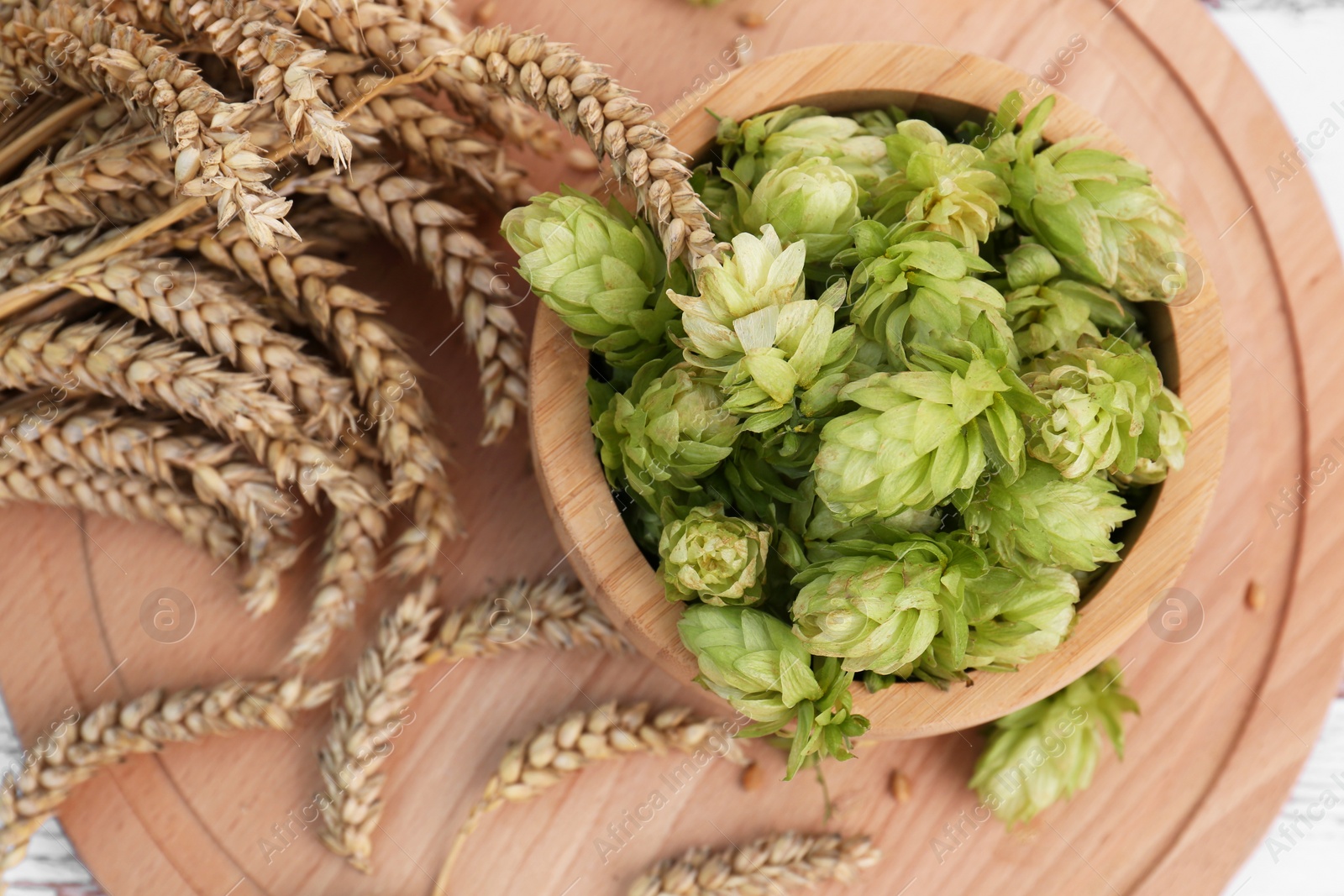 Photo of Fresh green hops and ears of wheat on wooden board, flat lay