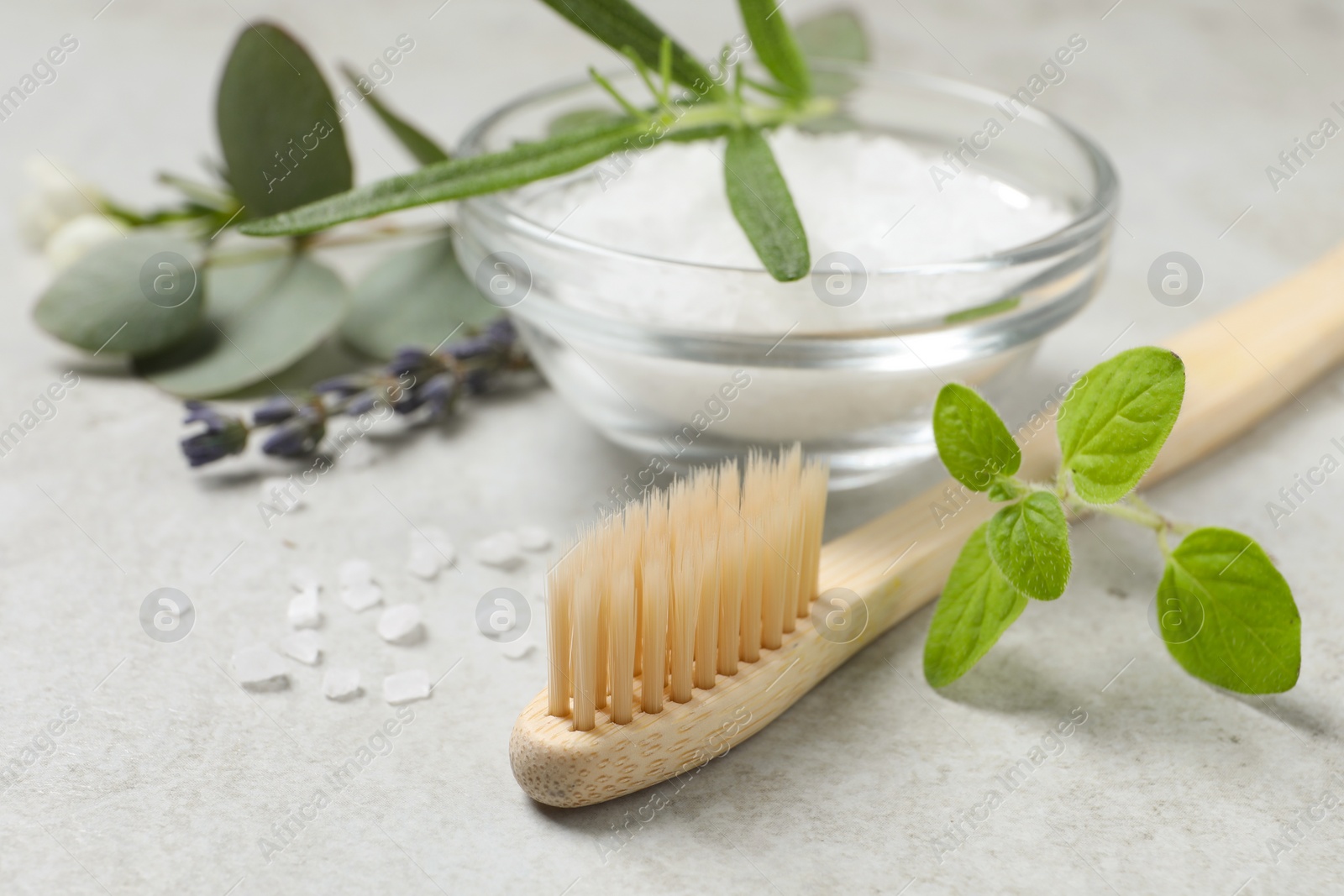 Photo of Bamboo toothbrush, sea salt and herbs on light grey table, closeup