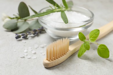Photo of Bamboo toothbrush, sea salt and herbs on light grey table, closeup