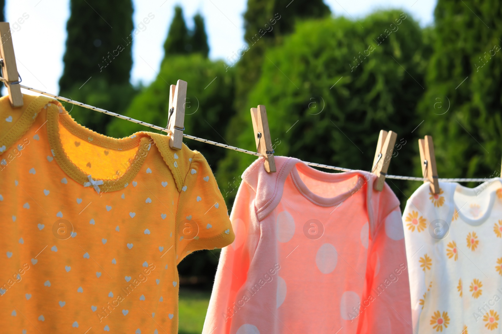 Photo of Clean baby onesies hanging on washing line in garden, closeup. Drying clothes