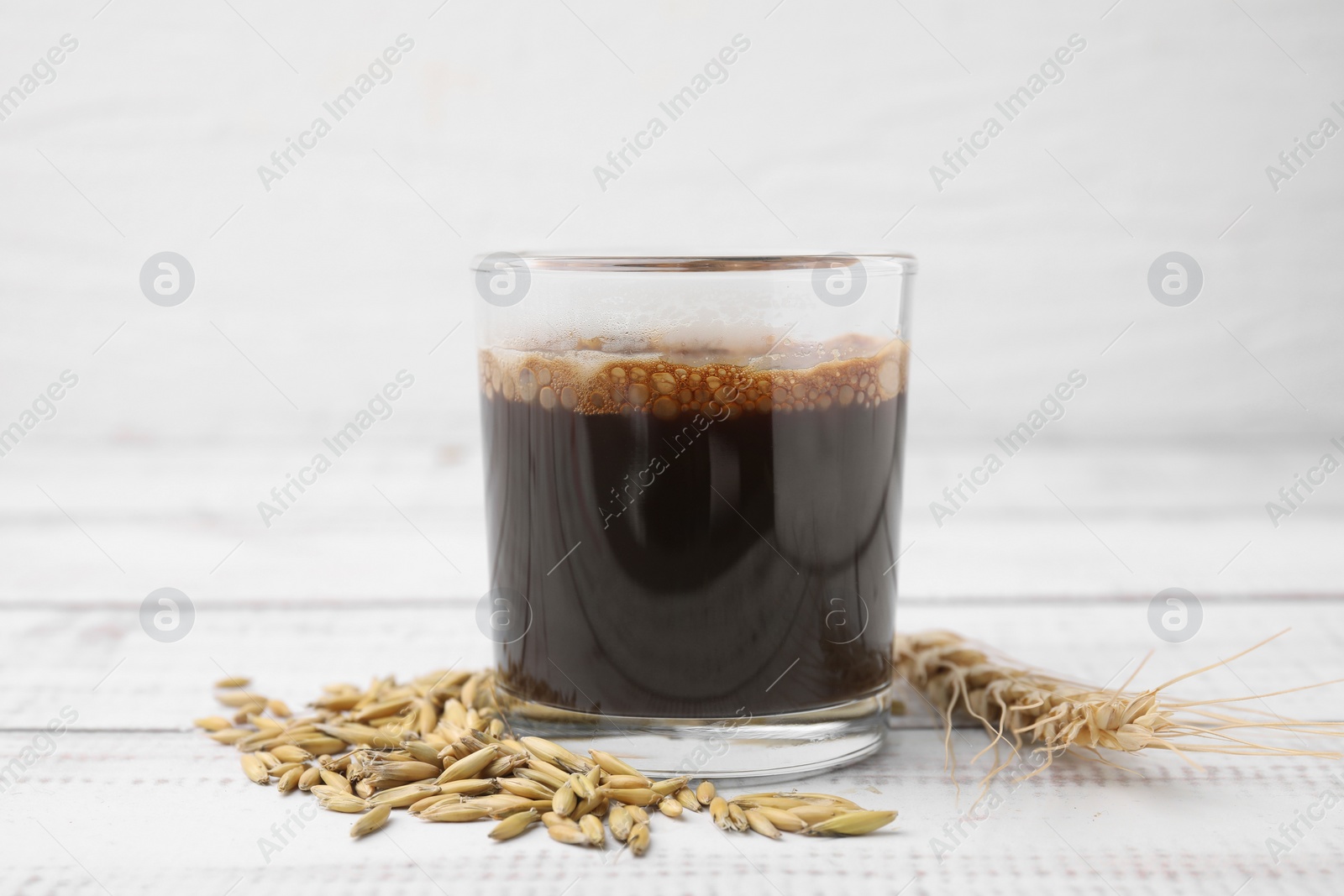 Photo of Cup of barley coffee, grains and spike on white wooden table, closeup