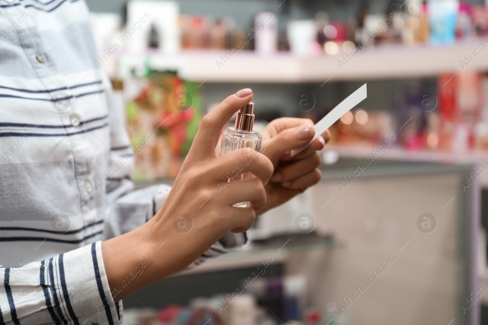 Photo of Young woman spraying perfume on blotter in shop, closeup