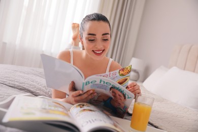 Photo of Happy woman reading magazine on bed indoors