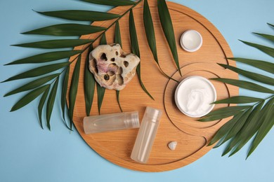Photo of Different cosmetic products, palm leaves and stones on light blue background, flat lay