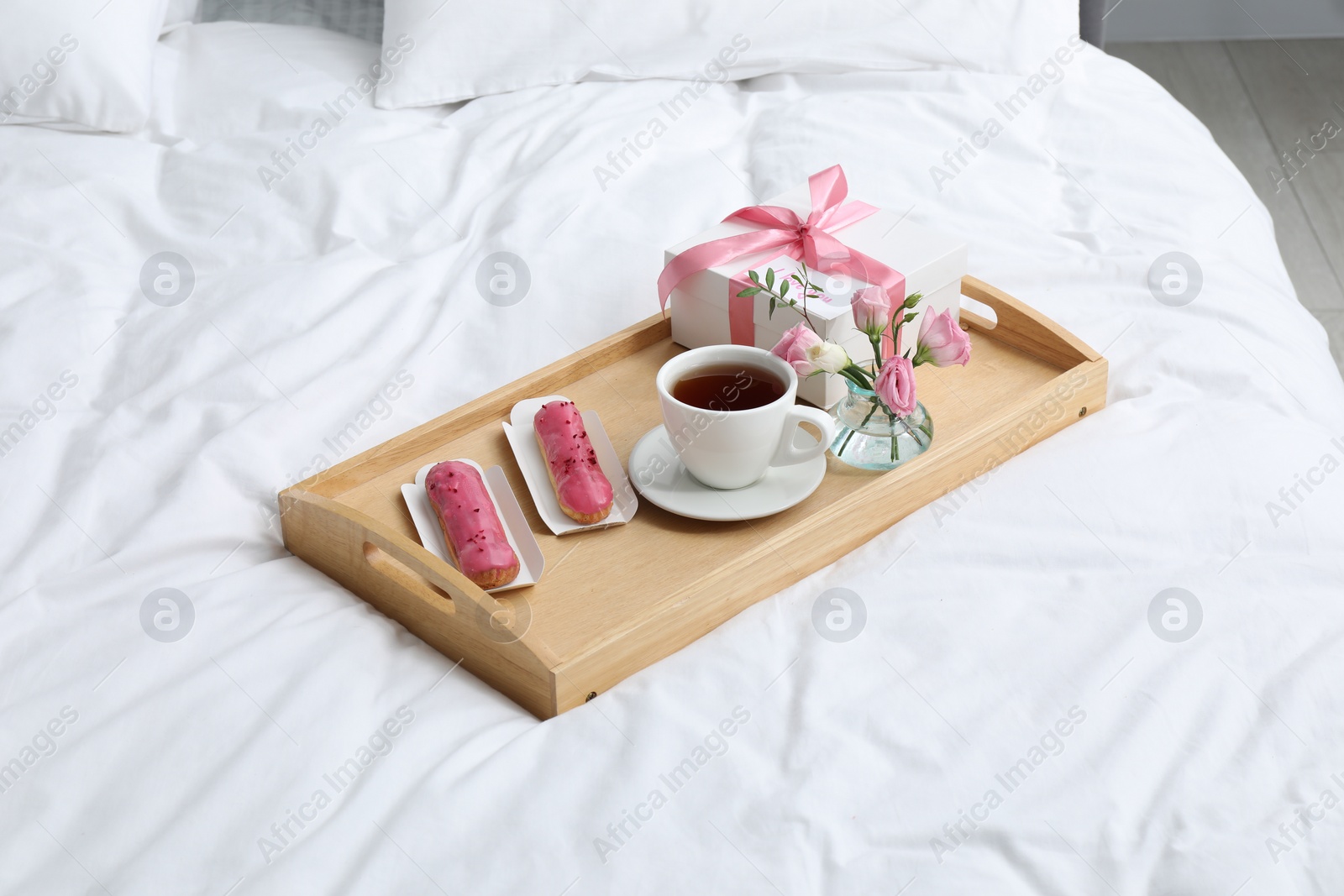 Photo of Tasty breakfast served in bed. Delicious eclairs, tea, gift box, flowers and card with phrase I Love You on tray