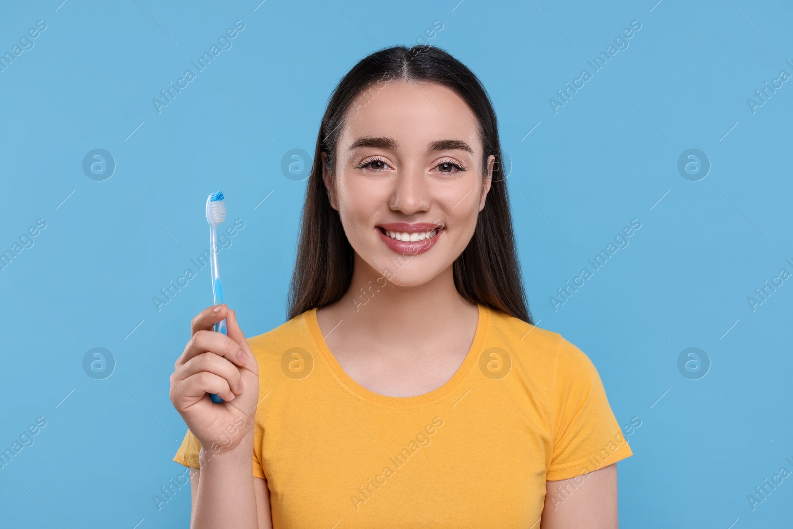 Photo of Happy young woman holding plastic toothbrush on light blue background