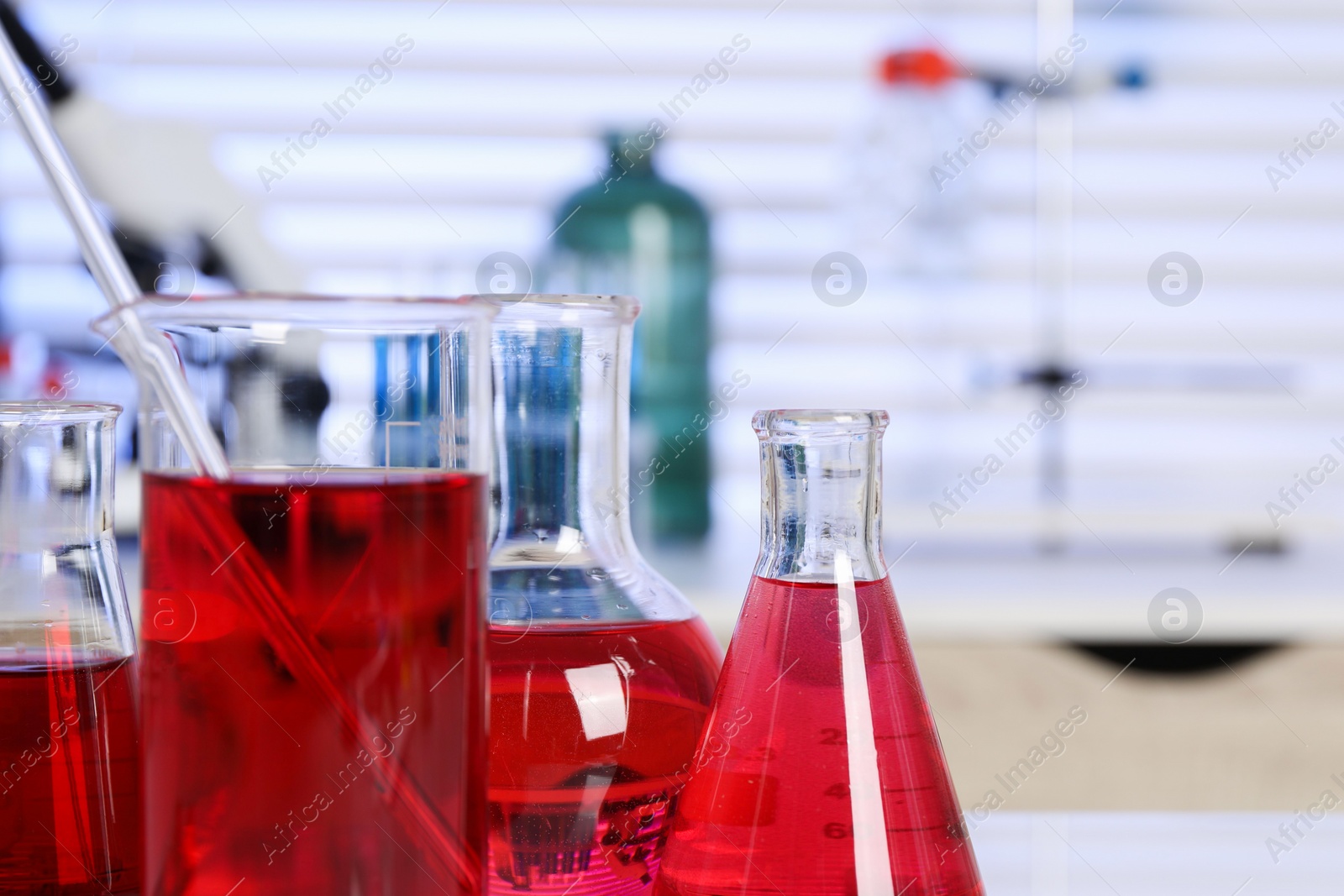 Photo of Laboratory analysis. Different glassware with red liquid on table indoors, closeup. Space for text