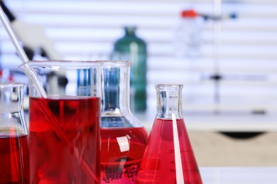 Photo of Laboratory analysis. Different glassware with red liquid on table indoors, closeup. Space for text