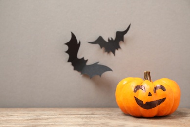 Photo of Pumpkin with scary face near decorative bats on grey background, space for text. Happy Halloween