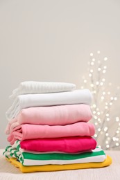 Photo of Stack of folded clothes on wooden table against beige background with blurred lights, space for text