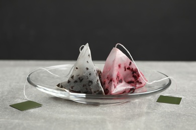 Saucer with different used pyramid tea bags on light grey table, closeup