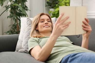 Photo of Woman reading book on sofa in room with houseplants