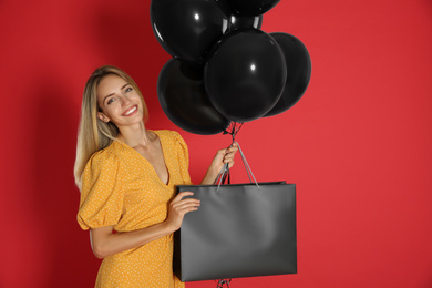 Happy young woman with balloons and shopping bag on red background. Black Friday Sale