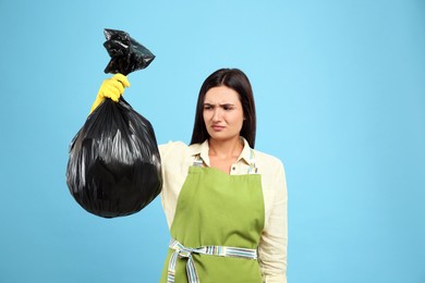 Photo of Woman holding full garbage bag on light blue background