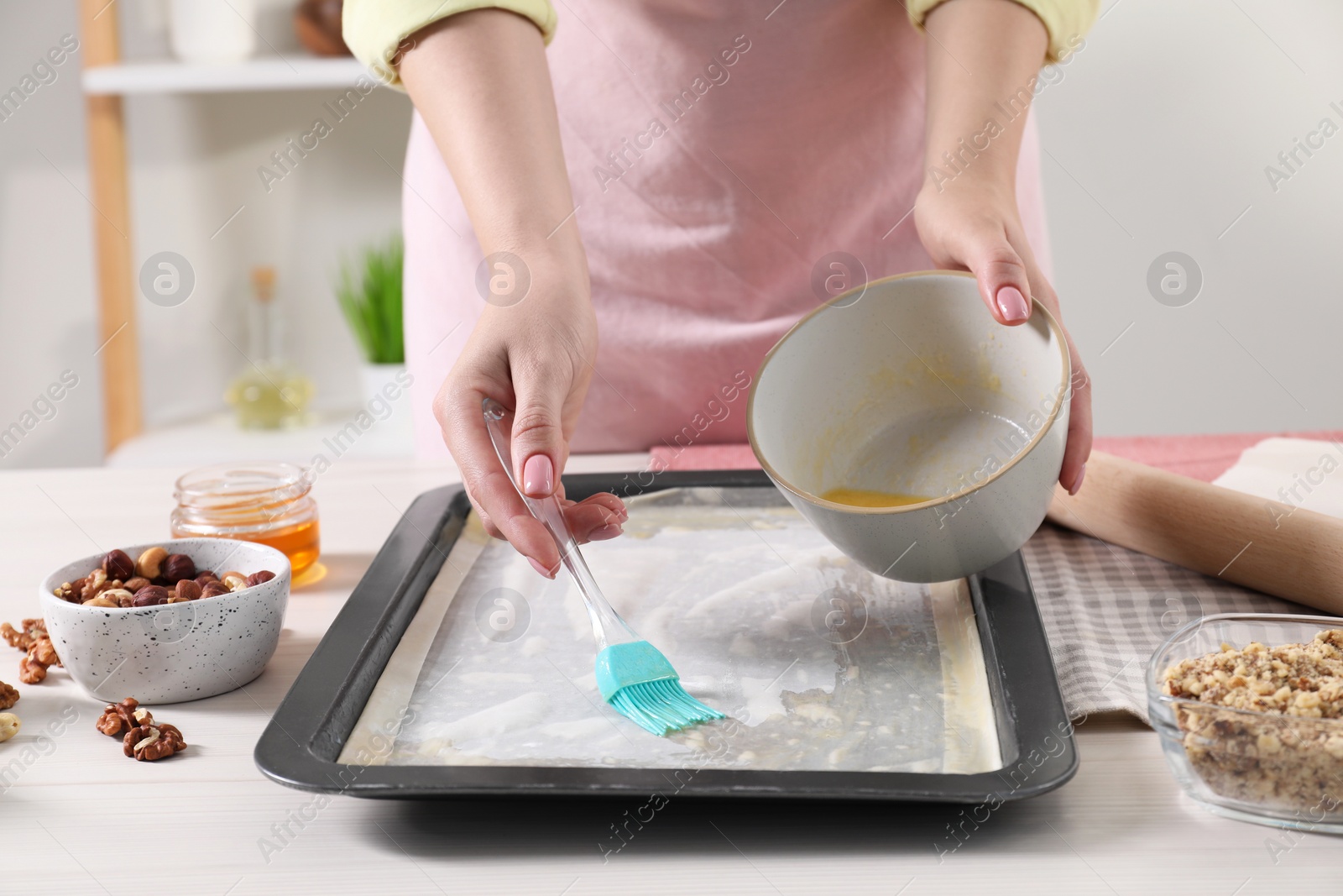 Photo of Making delicious baklava. Woman buttering dough in baking pan at white wooden table, closeup