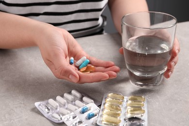 Woman with different pills and glass of water at grey table, closeup