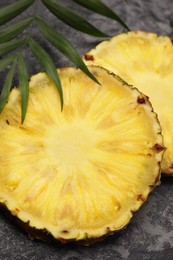 Slices of tasty ripe pineapple and green leaves on black textured table, closeup