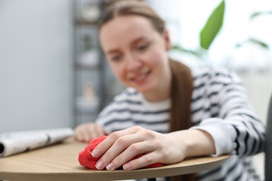 Photo of Woman cleaning wooden coffee table with rag at home, selective focus