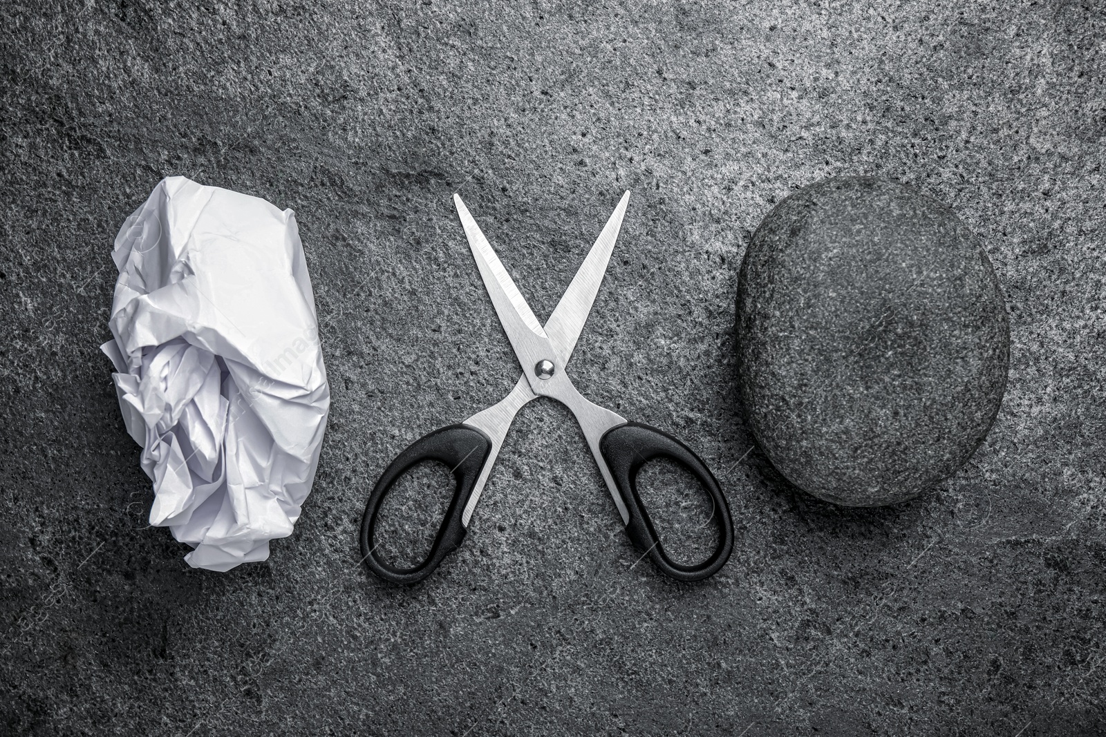 Photo of Rock, crumpled paper and scissors on dark grey textured table, flat lay