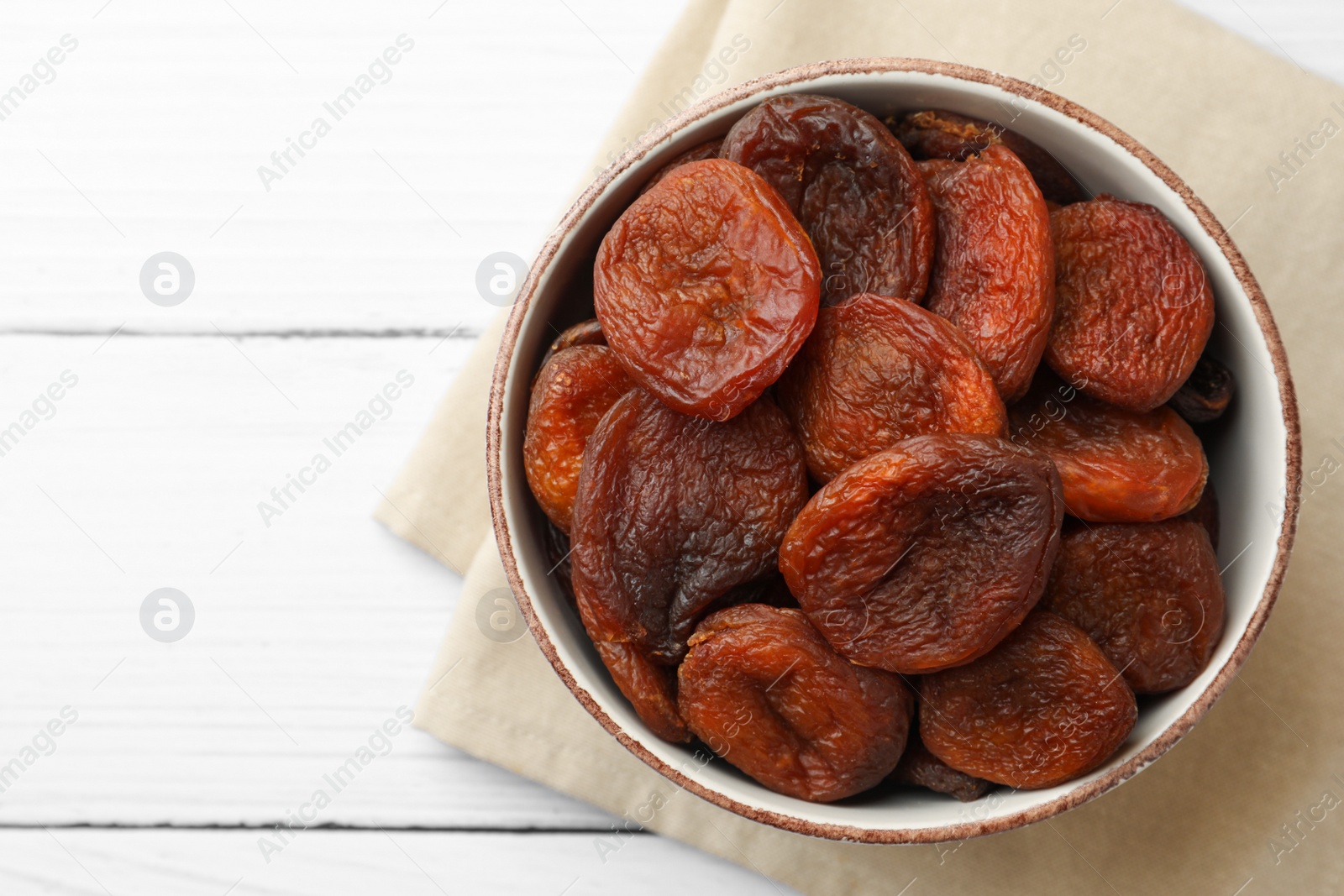 Photo of Bowl of tasty apricots and space for text on white wooden table, top view. Dried fruits