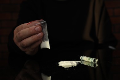 Photo of Drug addiction. Man with cocaine and rolled dollar banknote at black table, closeup