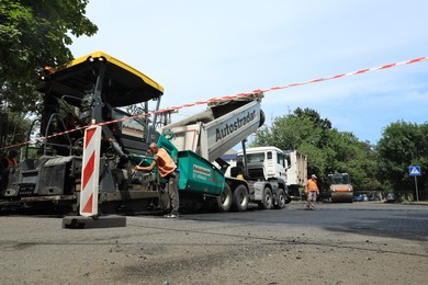 Photo of MYKOLAIV, UKRAINE - AUGUST 04, 2021: Workers with road repair machinery laying new asphalt