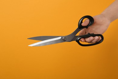 Woman holding tailor's scissors on yellow background, closeup