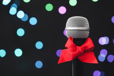 Photo of Microphone with red bow against blurred lights, space for text. Christmas music
