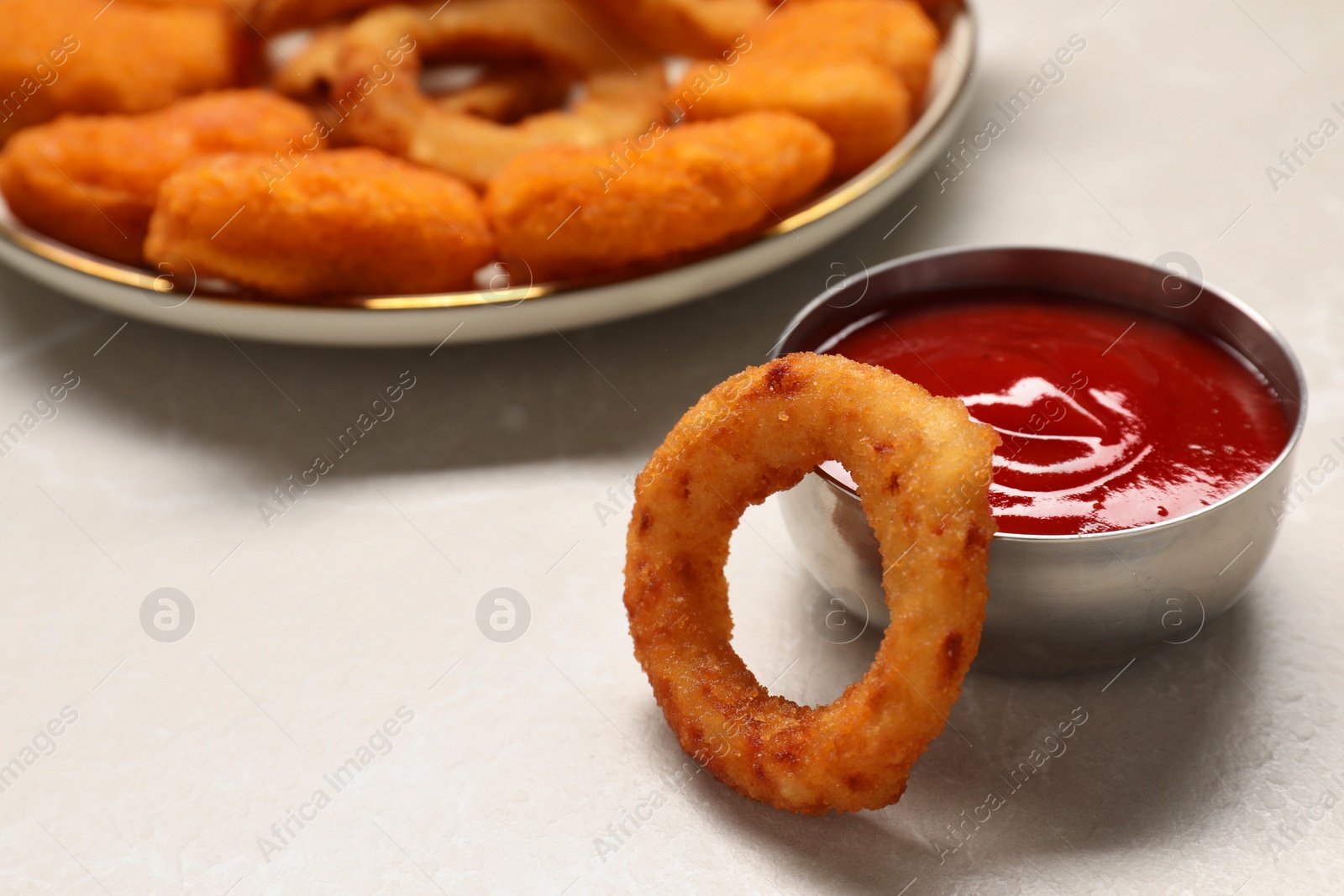 Photo of Tasty fried onion rings and ketchup on light grey marble table, closeup. Space for text