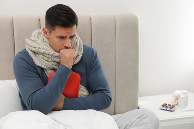 Photo of Ill man with hot water bottle coughing at home