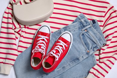 New stylish red sneakers, jeans, striped sweater and bag on white background, flat lay. Casual outfit