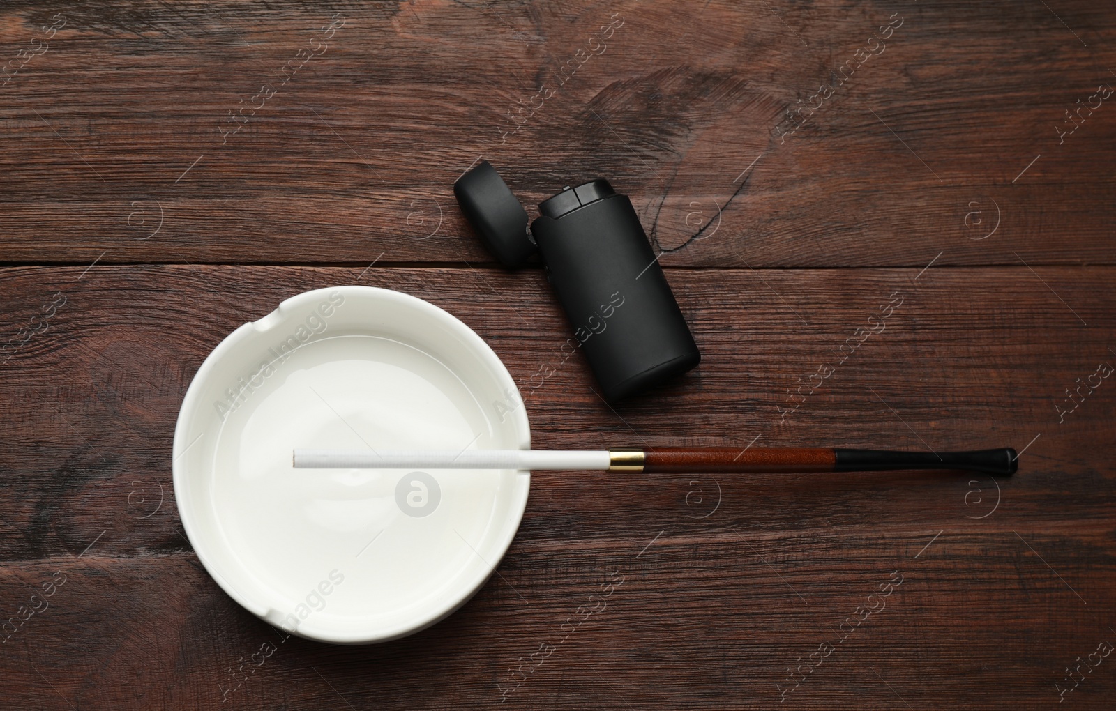 Photo of Ashtray with long cigarettes holder and lighter on wooden table, flat lay. Space for text