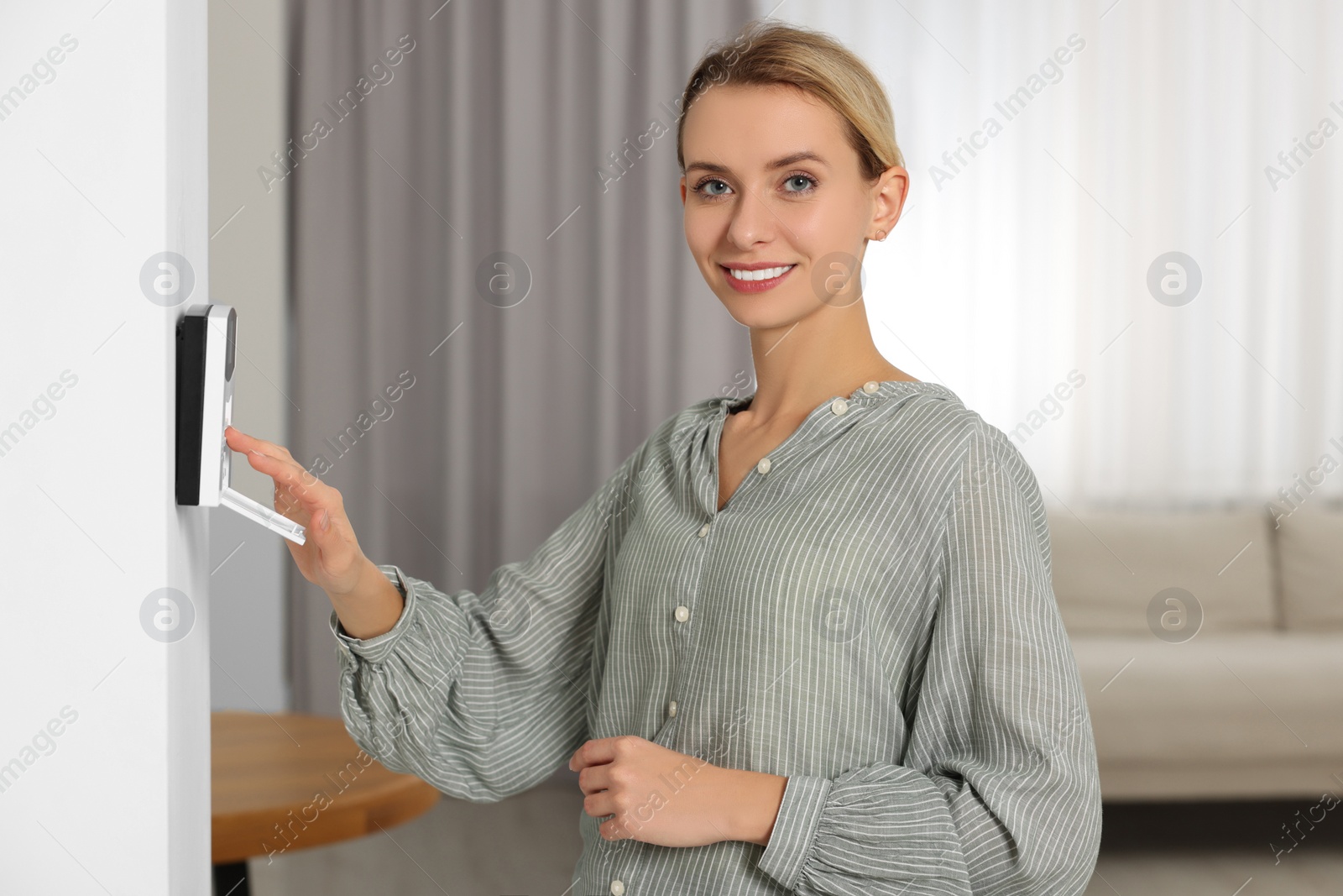 Photo of Smiling woman entering code on home security system in room