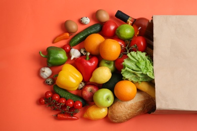 Photo of Paper bag with different groceries on coral background, flat lay