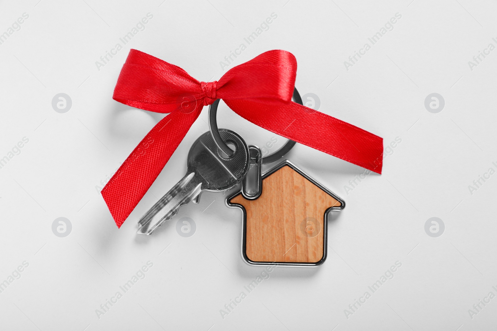 Photo of Key with trinket in shape of house and red bow on light grey background, top view. Housewarming party