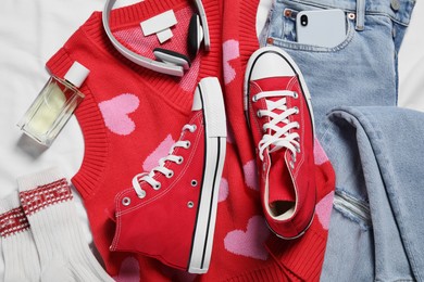 Photo of Pair of stylish red shoes, clothes and smartphone on white fabric, flat lay