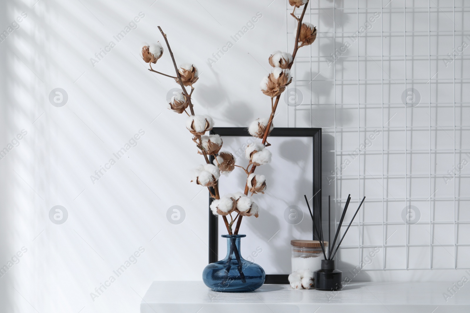 Photo of Reed diffuser, candle and cotton branches with fluffy flowers on white wooden table indoors