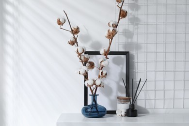 Reed diffuser, candle and cotton branches with fluffy flowers on white wooden table indoors