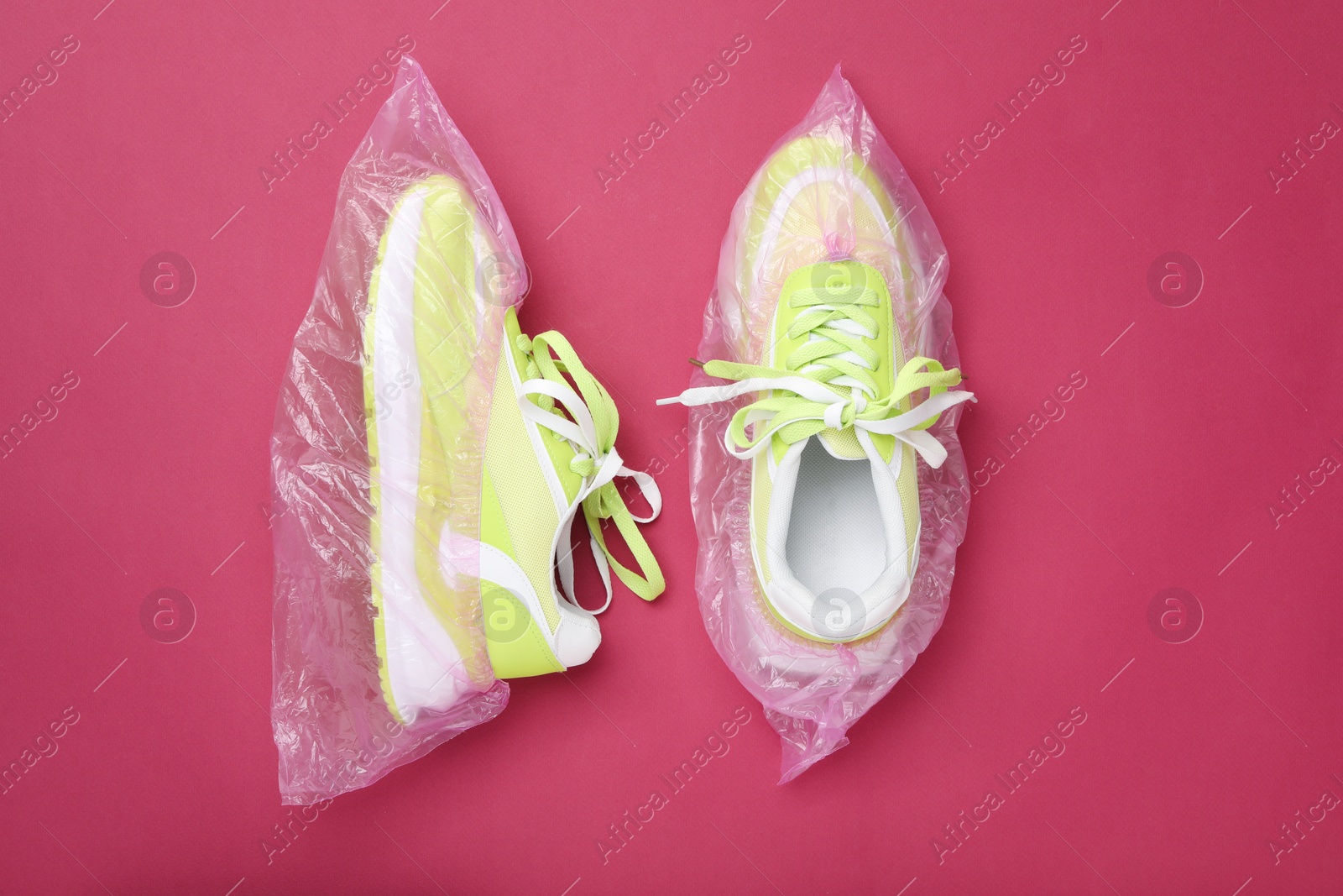 Photo of Sneakers in shoe covers on pink background, top view