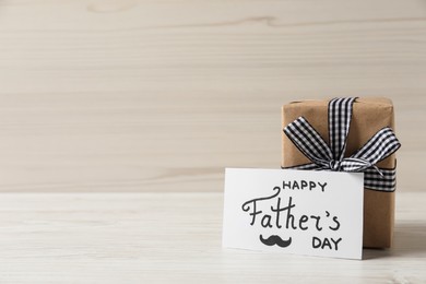 Photo of Card with phrase Happy Father's Day and gift box on white wooden background. Space for text