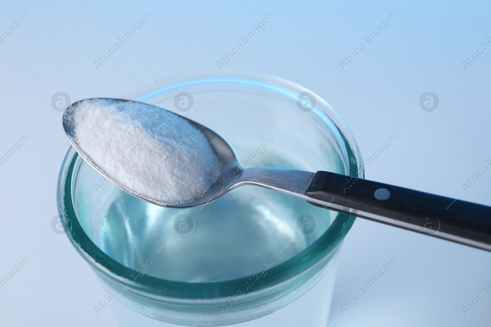 Photo of Glass of water and spoon with baking soda on light blue background, closeup