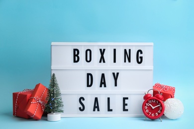 Photo of Lightbox with phrase BOXING DAY SALE and Christmas decorations on light blue background