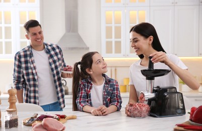 Photo of Happy family making dinner together in kitchen, woman using modern meat grinder