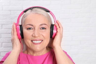 Mature woman enjoying music in headphones against brick wall. Space for text